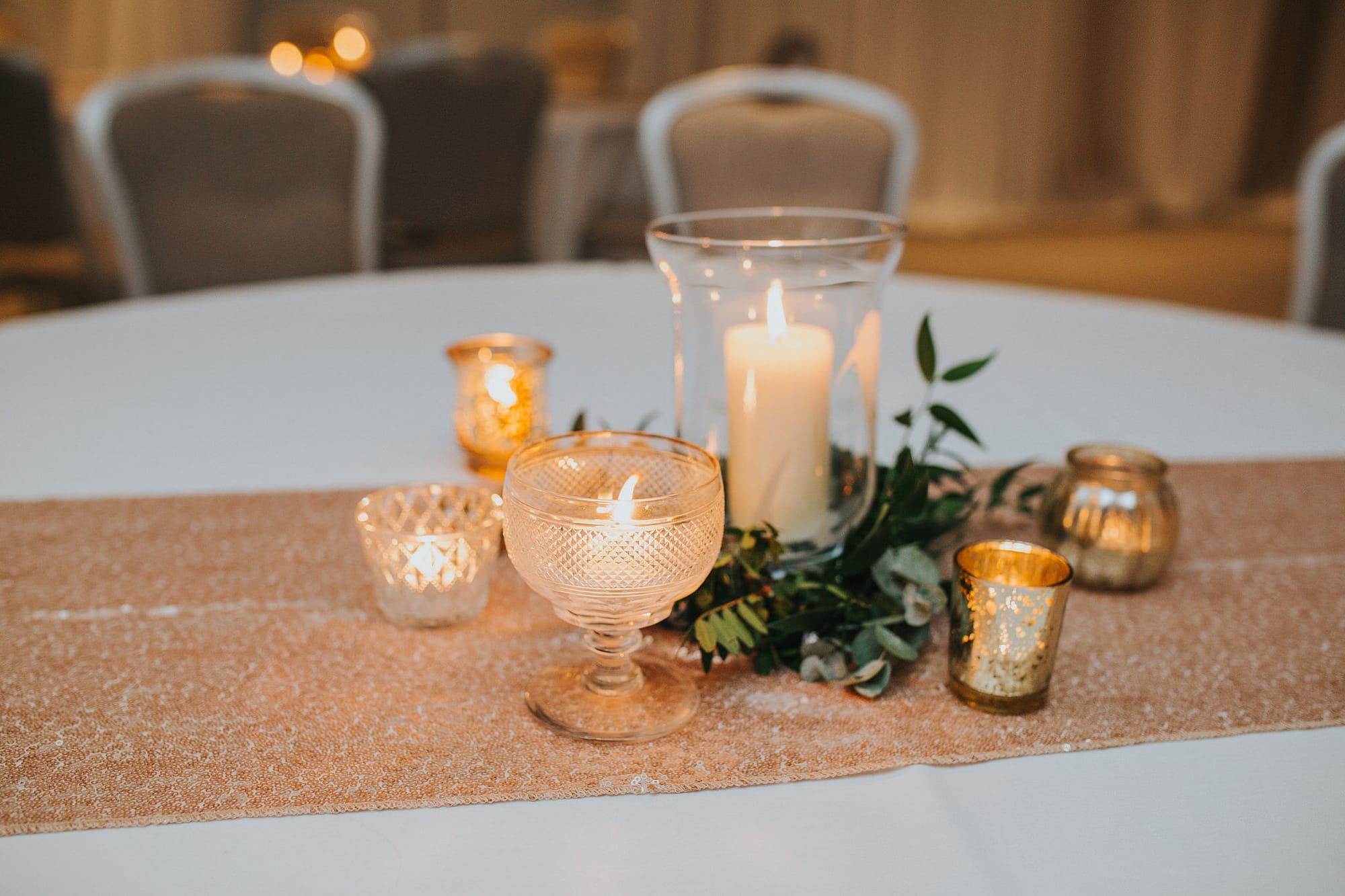 tealights and storm lantern wedding table centres with greenery and gold table runner