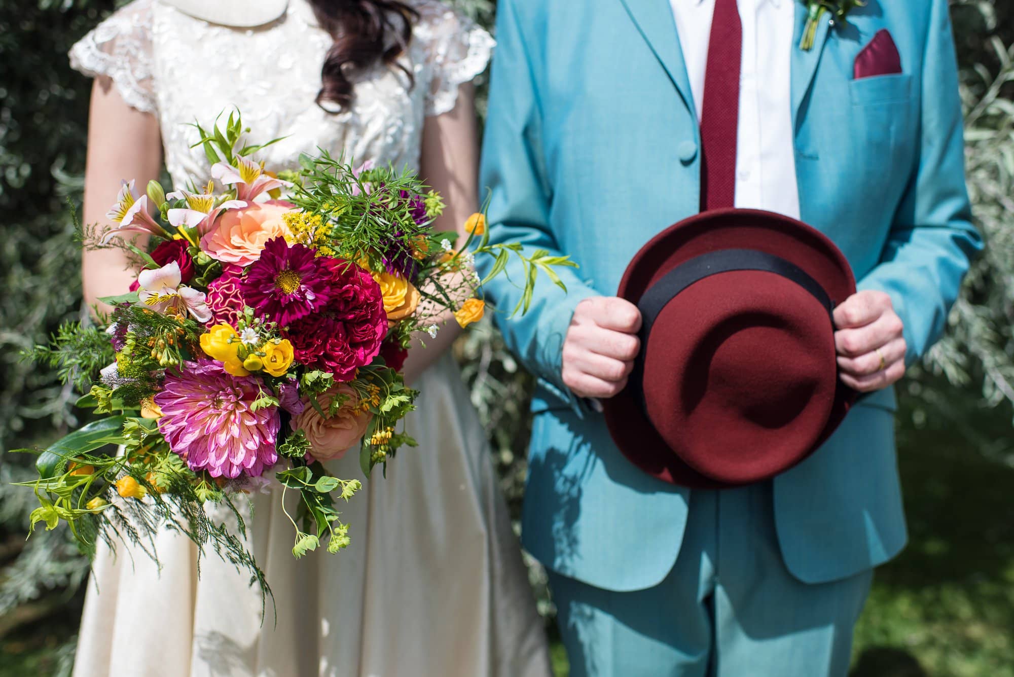 bride and groom with colourful bouquet and burgundy hat
