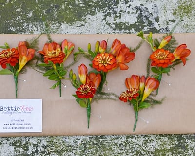 Orange freesia and zinnia buttonholes. Wedding flowers Brighton.